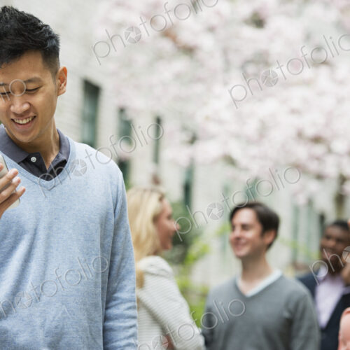 City life in spring. Young people outdoors in a city park. A man checking his cell… City life in spring. Young people outdoors in a city park. A man checking his cell…