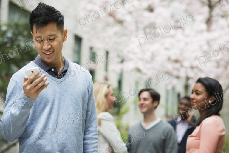 City life in spring. Young people outdoors in a city park. A man checking his cell…