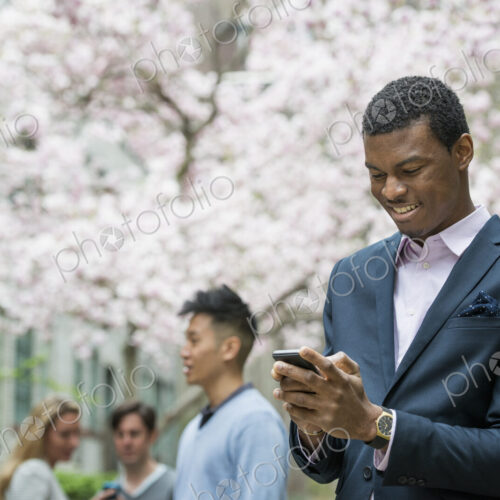 City life in spring. Young people outdoors in a city park. A man checking his cell… City life in spring. Young people outdoors in a city park. A man checking his cell…