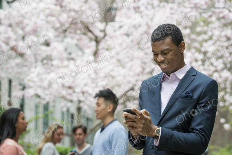 City life in spring. Young people outdoors in a city park. A man checking his cell…