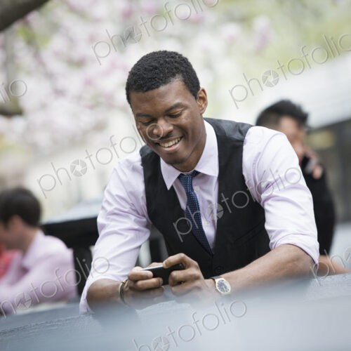 City life in spring. Young people outdoors in a city park. A man sitting down checking…