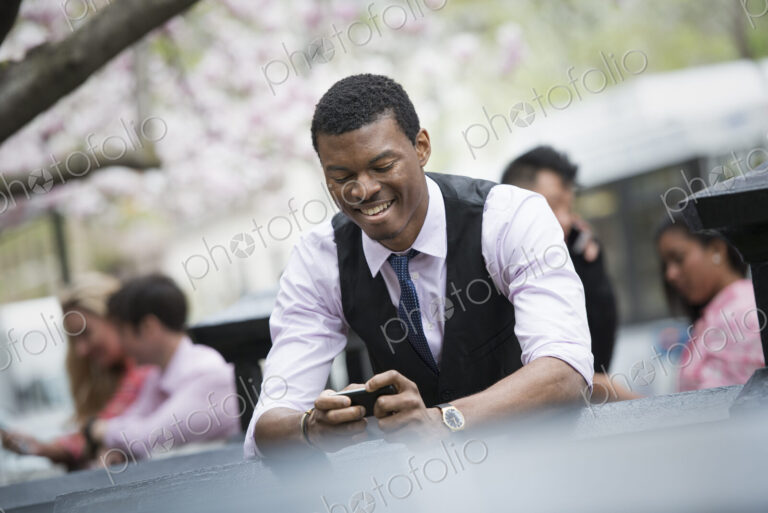 City life in spring. Young people outdoors in a city park. A man sitting down checking…