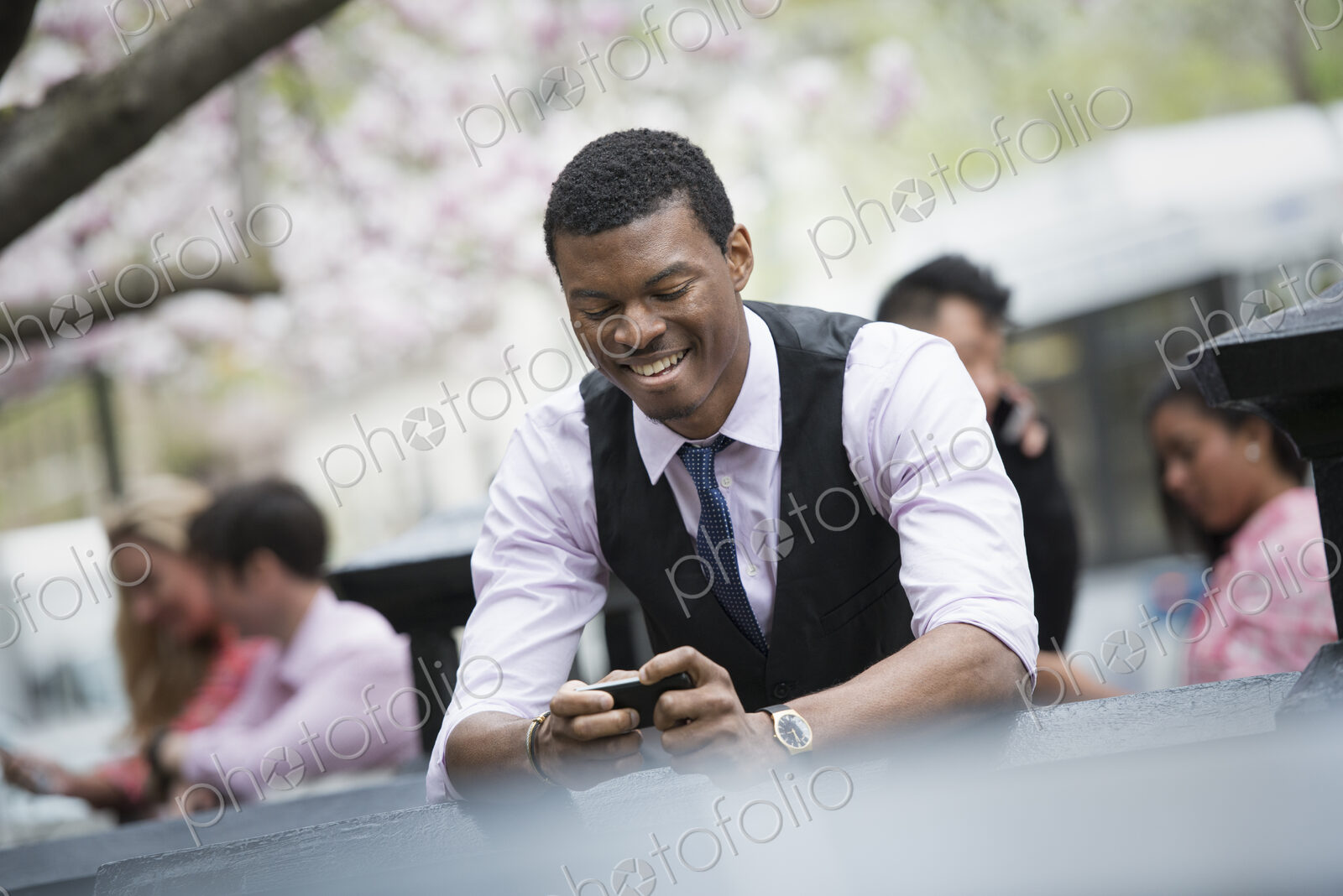 City life in spring. Young people outdoors in a city park. A man sitting down checking…
