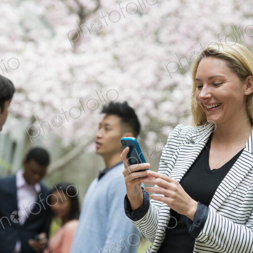 City life in spring. Young people outdoors in a city park. A woman using her cell… City life in spring. Young people outdoors in a city park. A woman using her cell…