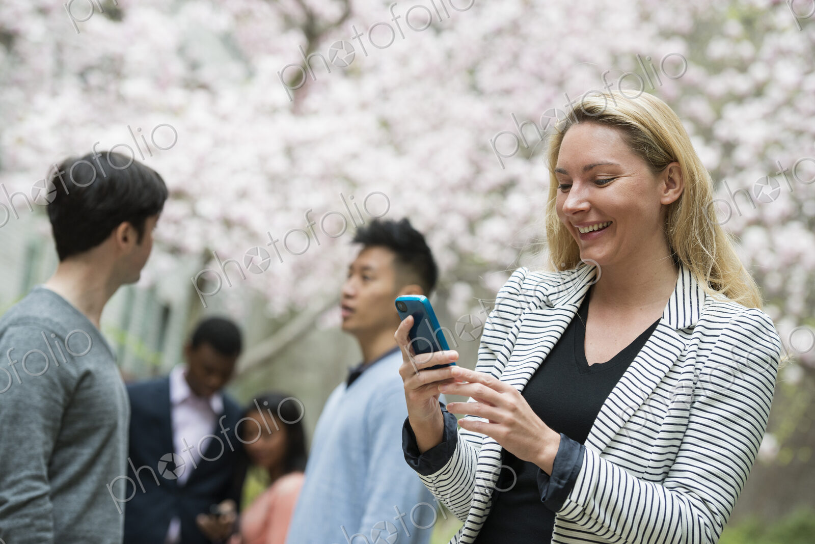 City life in spring. Young people outdoors in a city park. A woman using her cell…