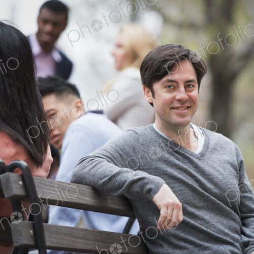 City life in spring. Young people outdoors in a city park. Sitting on a park bench. A…