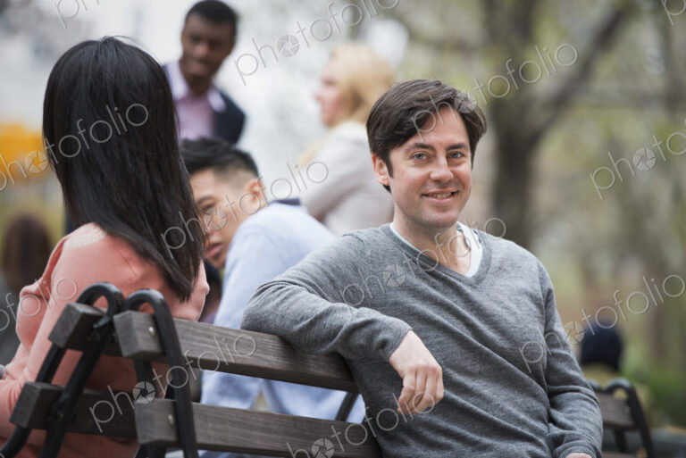 City life in spring. Young people outdoors in a city park. Sitting on a park bench. A…