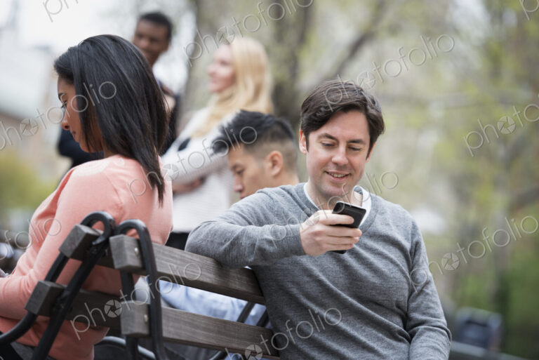 City life in spring. Young people outdoors in a city park. Sitting on a park bench.…