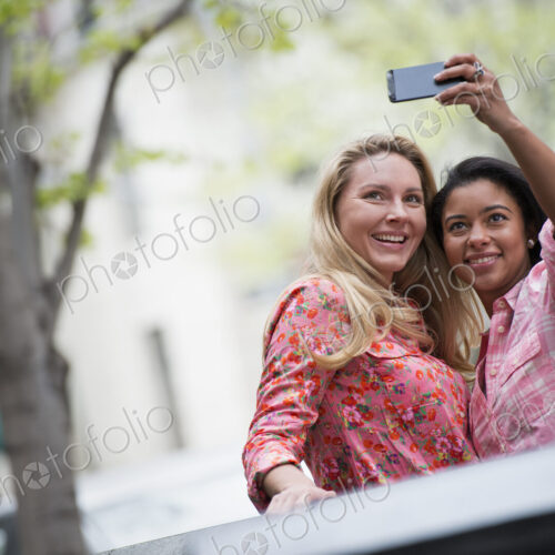 City life in spring. Young people outdoors in a city park. Two women taking a self…