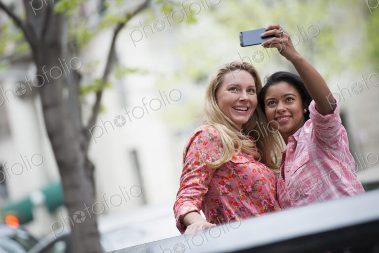City life in spring. Young people outdoors in a city park. Two women taking a self…