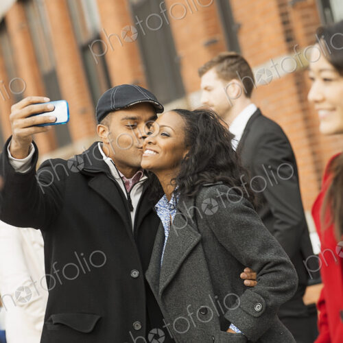 City life. A group of people on the go. A man holding out a camera phone and taking…