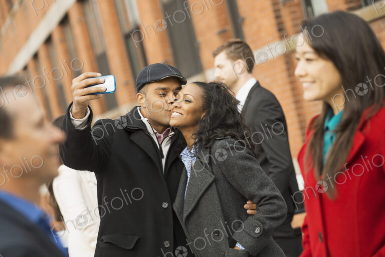 City life. A group of people on the go. A man holding out a camera phone and taking…