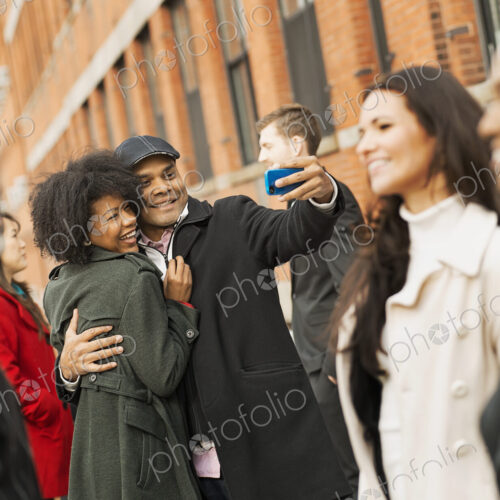 City life. A group of people on the go. A man holding out a camera phone and taking…