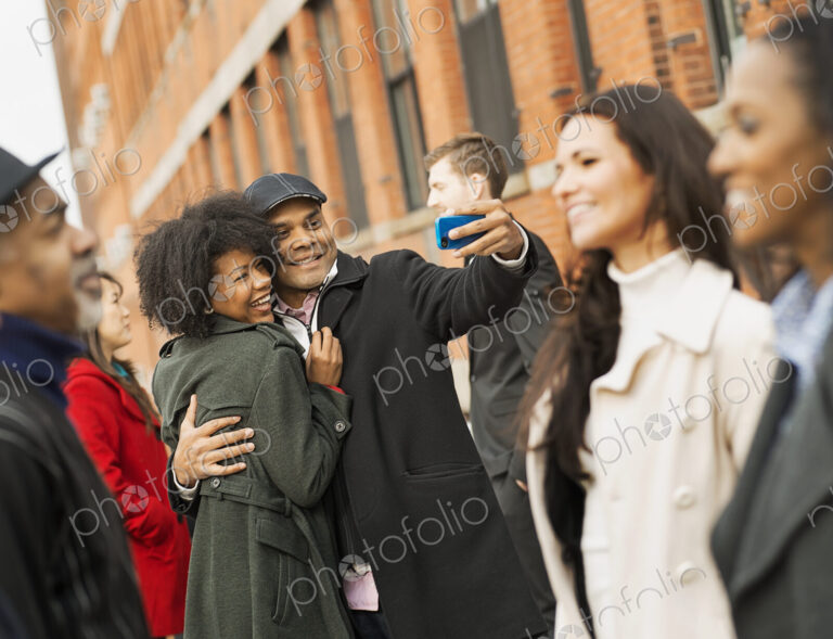 City life. A group of people on the go. A man holding out a camera phone and taking…
