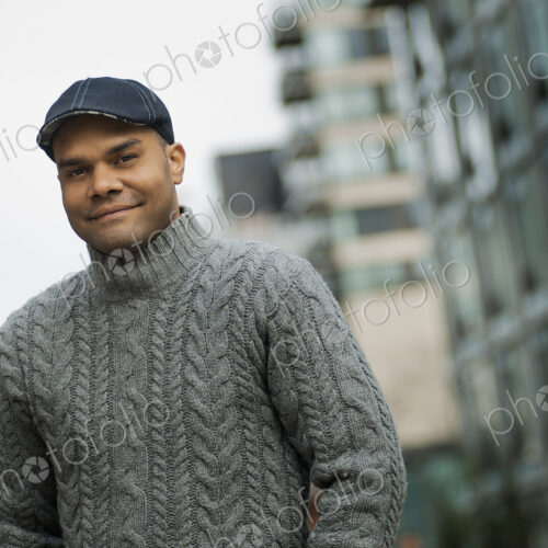 City life. A man in a flat hat, and jumper on the street of a city.
