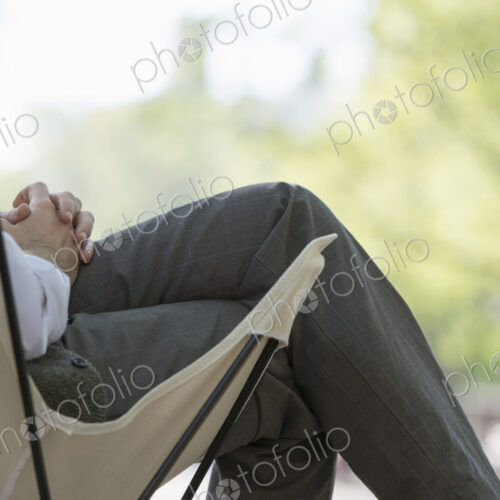 City life. A man sitting in a canvas camping chair in the park.
