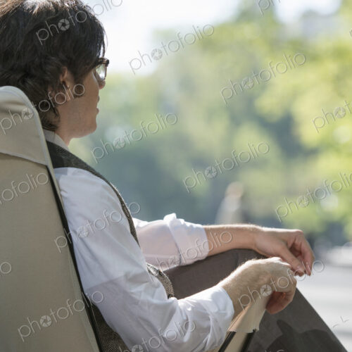 City life. A man sitting in a canvas camping chair in the park.