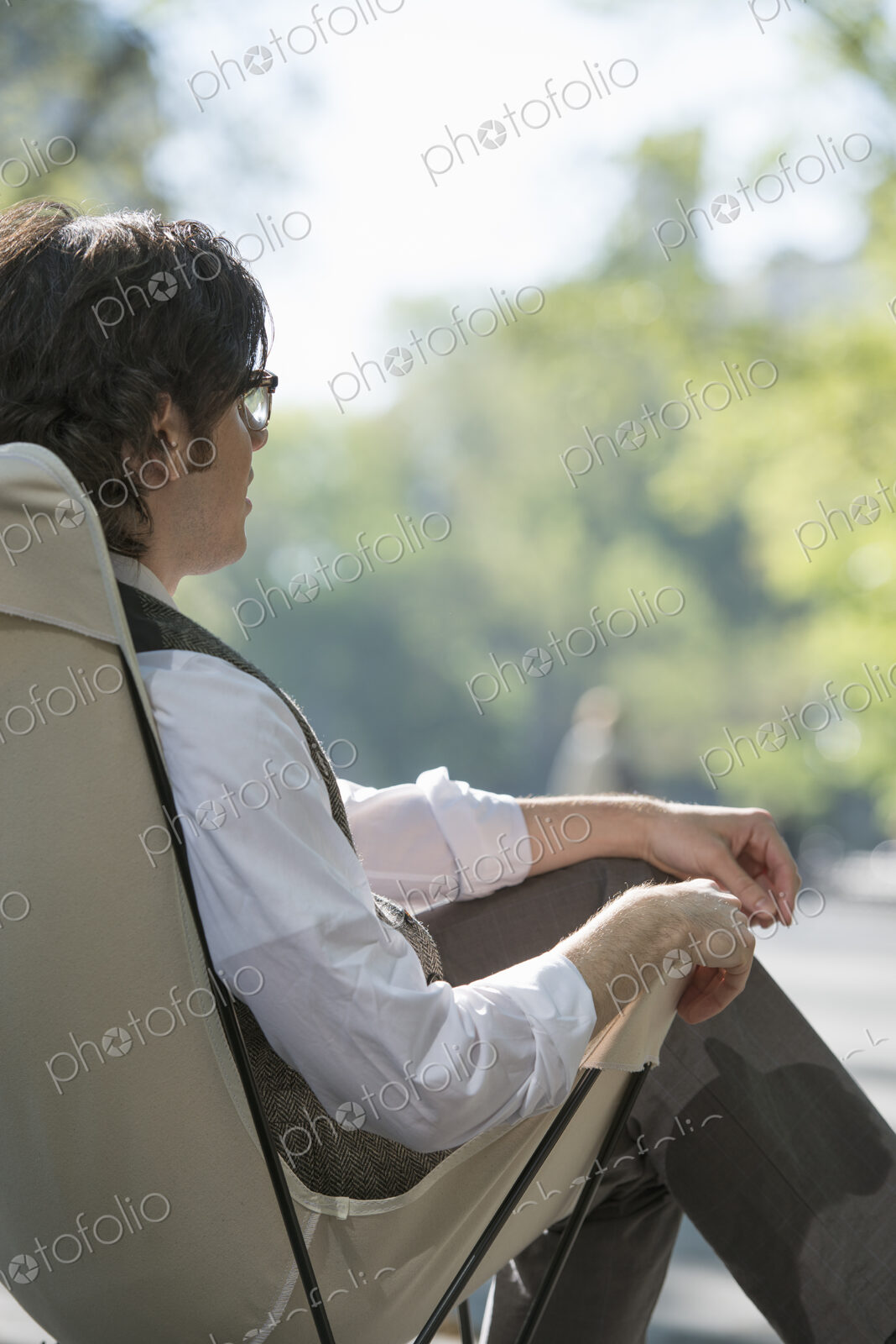 City life. A man sitting in a canvas camping chair in the park.