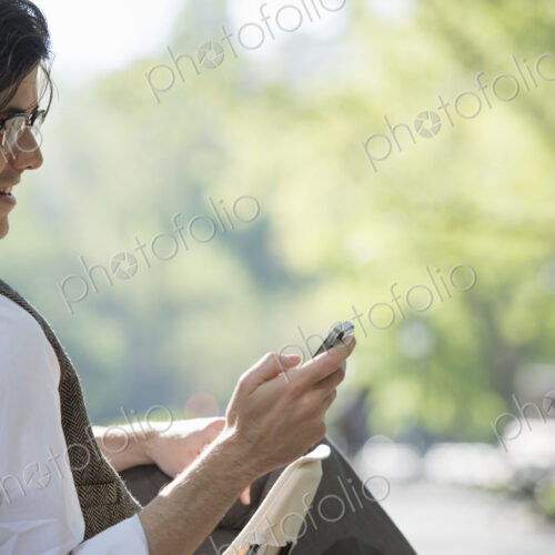 City life. A man sitting in a canvas camping chair in the park looking at his cell phone.