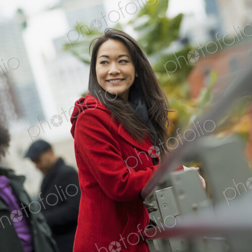 City life. A woman in a red winter coat leaning on a railing, taking time out. Two… City life. A woman in a red winter coat leaning on a railing, taking time out. Two…