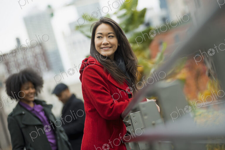 City life. A woman in a red winter coat leaning on a railing, taking time out. Two…