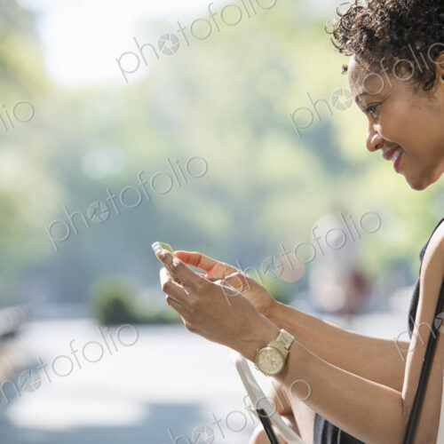 City life. A woman sitting in a camping chair in a city park, checking her cell phone.