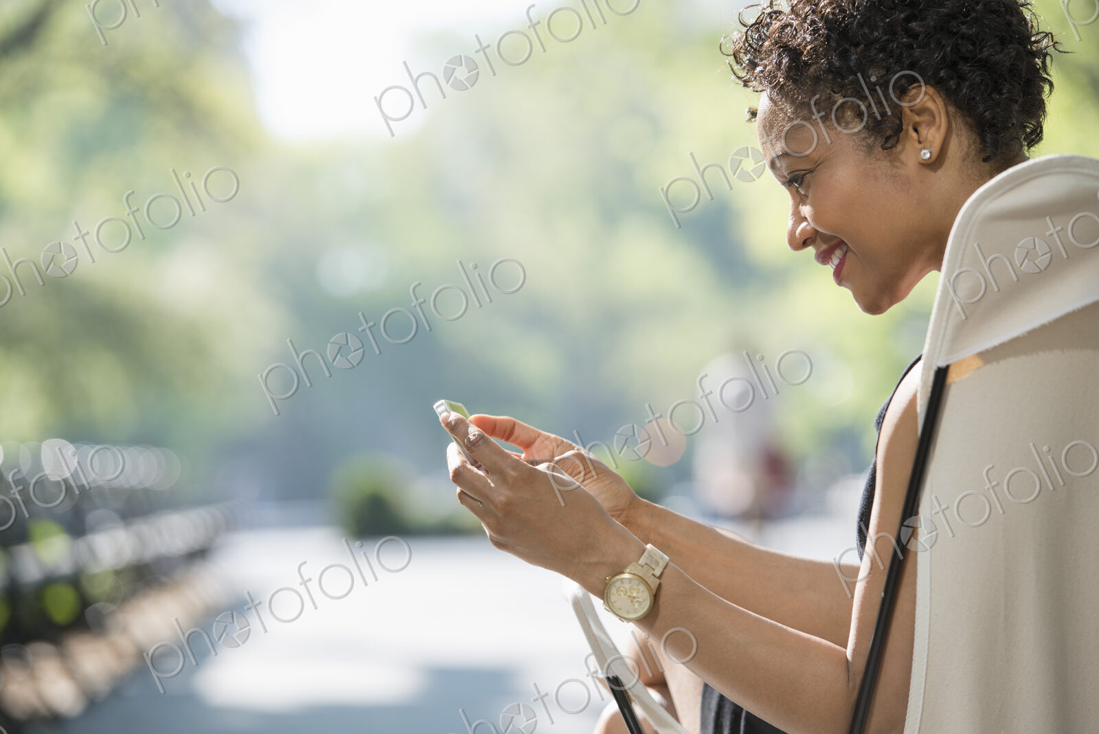 City life. A woman sitting in a camping chair in a city park, checking her cell phone.