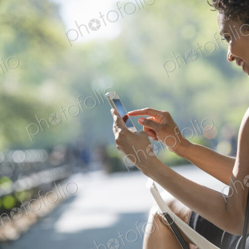 City life. A woman sitting in a camping chair in a city park, checking her cell phone.