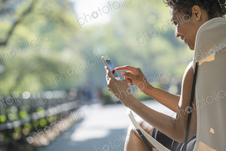 City life. A woman sitting in a camping chair in a city park, checking her cell phone.