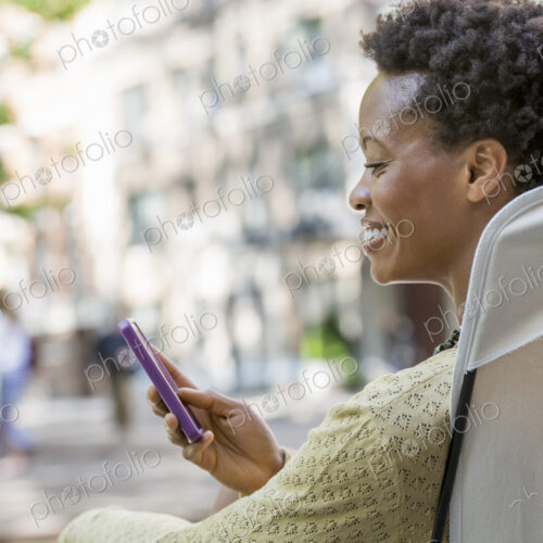 City life. A woman sitting in a camping chair in a city park, checking her cell phone.