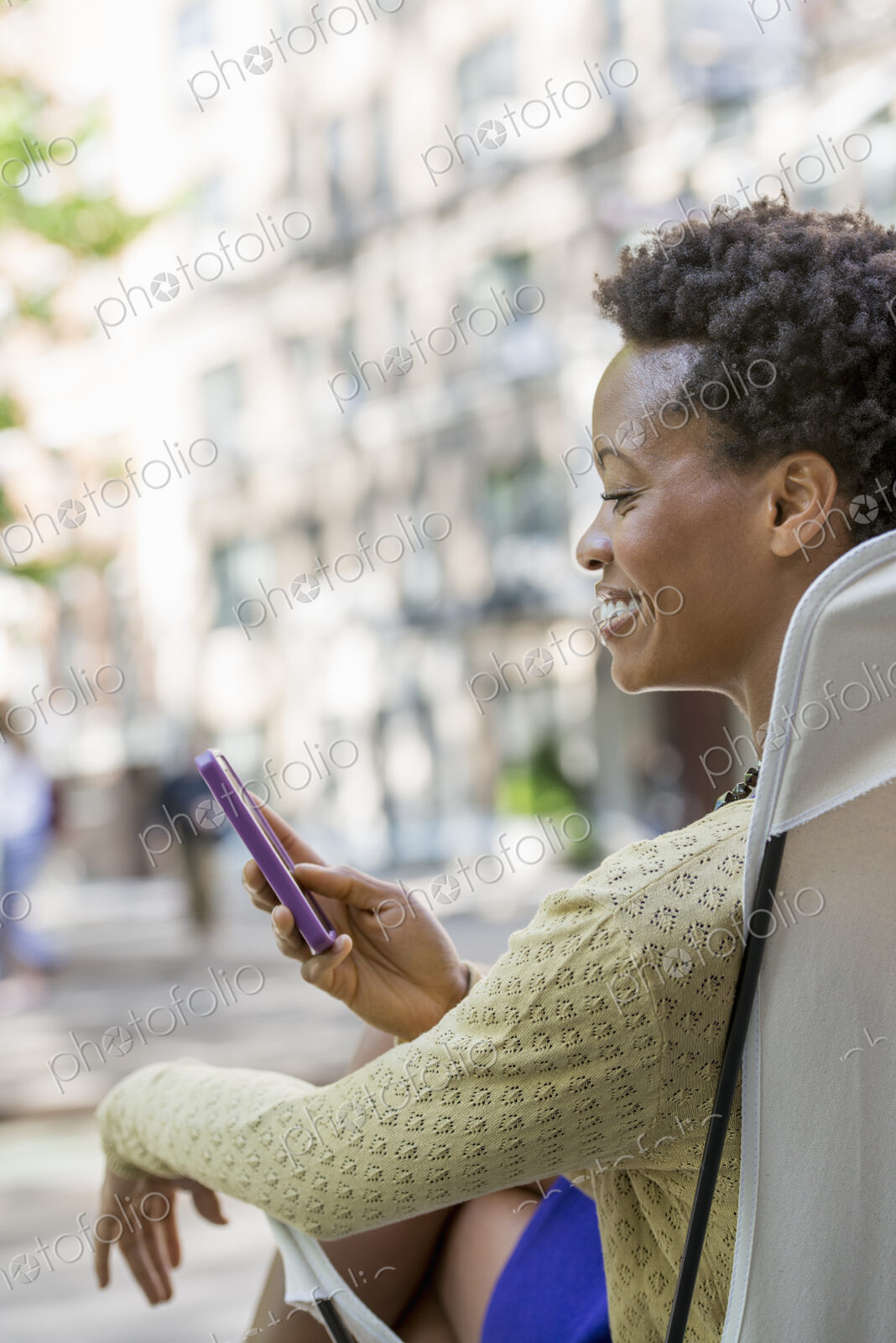 City life. A woman sitting in a camping chair in a city park, checking her cell phone.