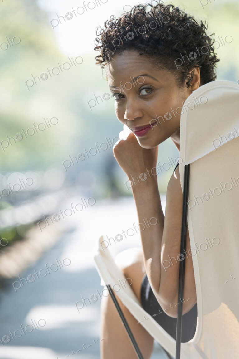 City life. A woman sitting in a camping chair in a city park, smiling and looking over…