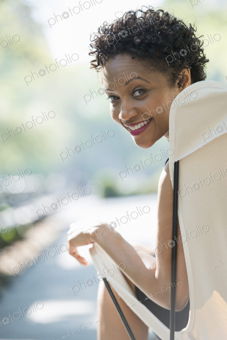 City life. A woman sitting in a camping chair in a city park, smiling and looking over…