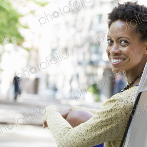City life. A woman sitting in a camping chair in a city park, smiling and looking over…