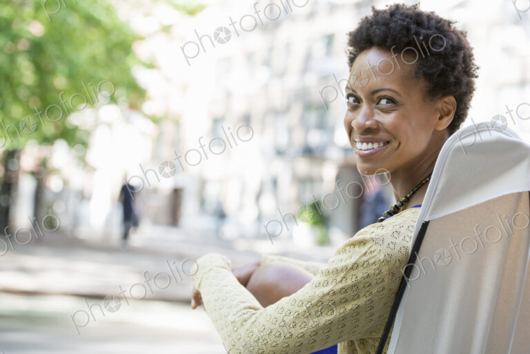 City life. A woman sitting in a camping chair in a city park, smiling and looking over…