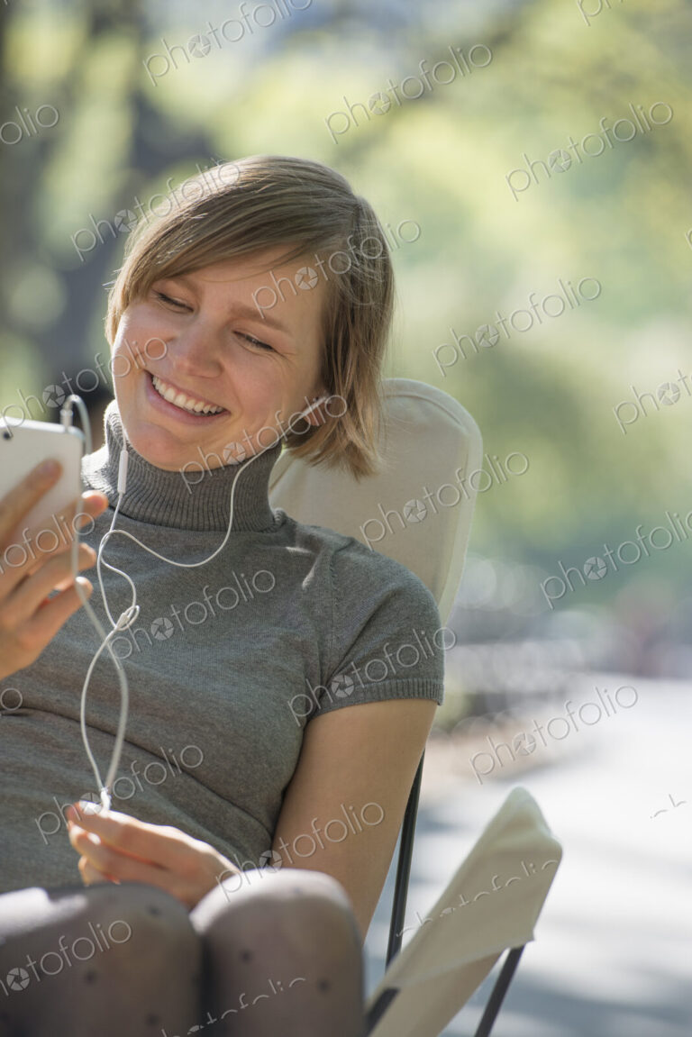 City life. A woman sitting in a camping chair in the park, listening to music wearing…
