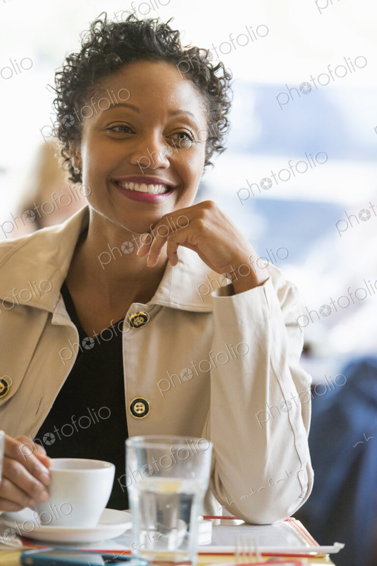 City life. A woman wearing a beige jacket sitting at a table in a cafe