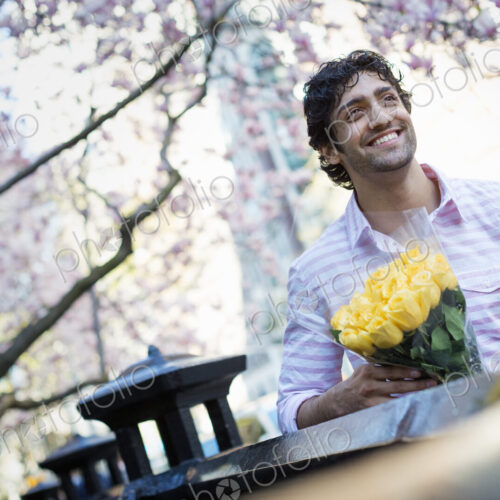 City life. A young man in the park in spring, holding a bunch of yellow roses.