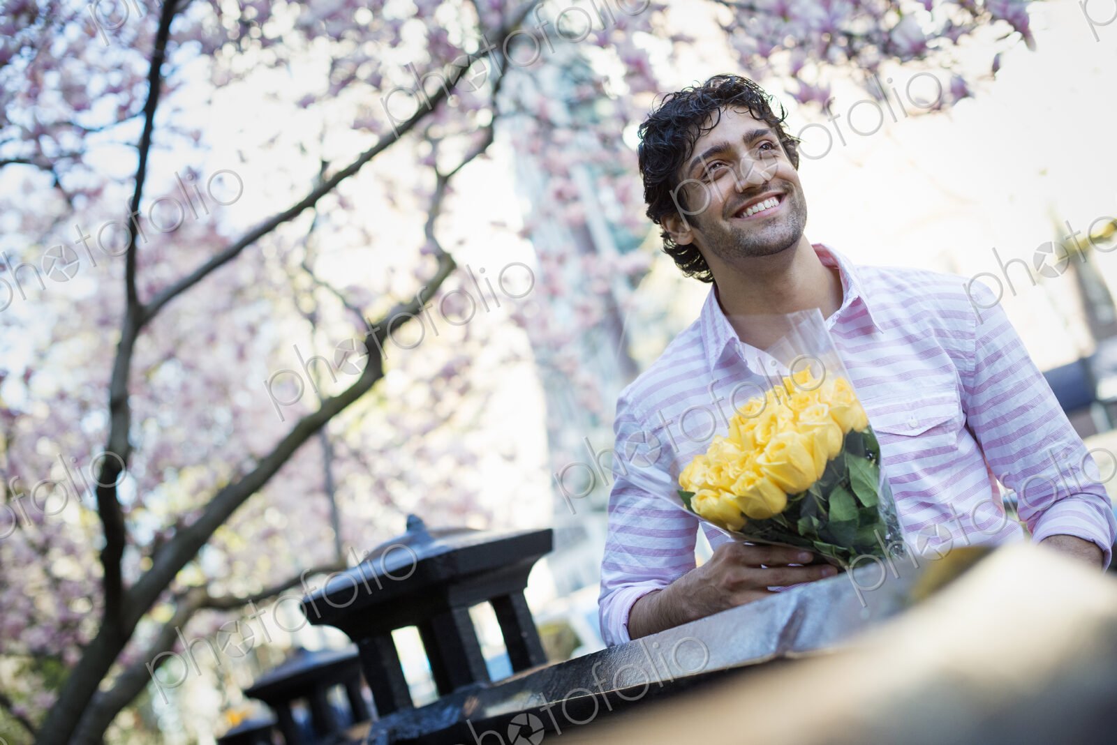City life. A young man in the park in spring, holding a bunch of yellow roses.