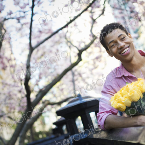 City life. A young man in the park in spring, holding a bunch of yellow roses.