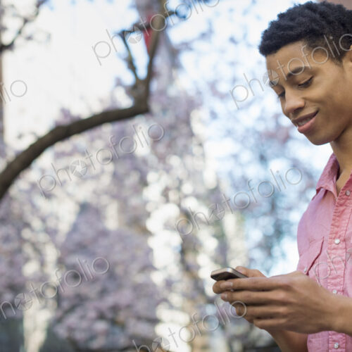 City life. A young man in the park in spring, using a mobile phone.
