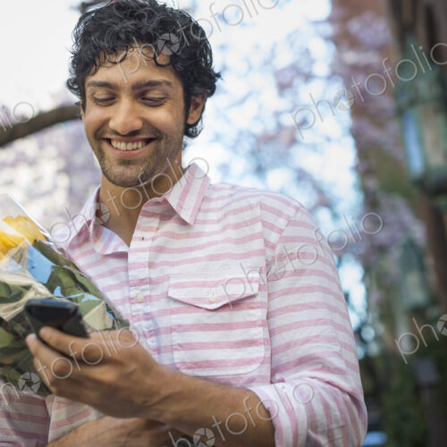 City life. A young man in the park in spring, using a mobile phone. Holding a bunch of…