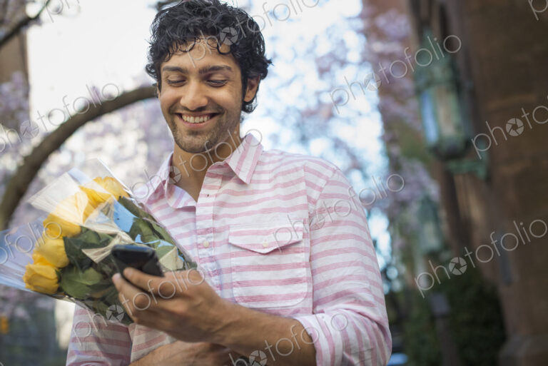City life. A young man in the park in spring, using a mobile phone. Holding a bunch of…