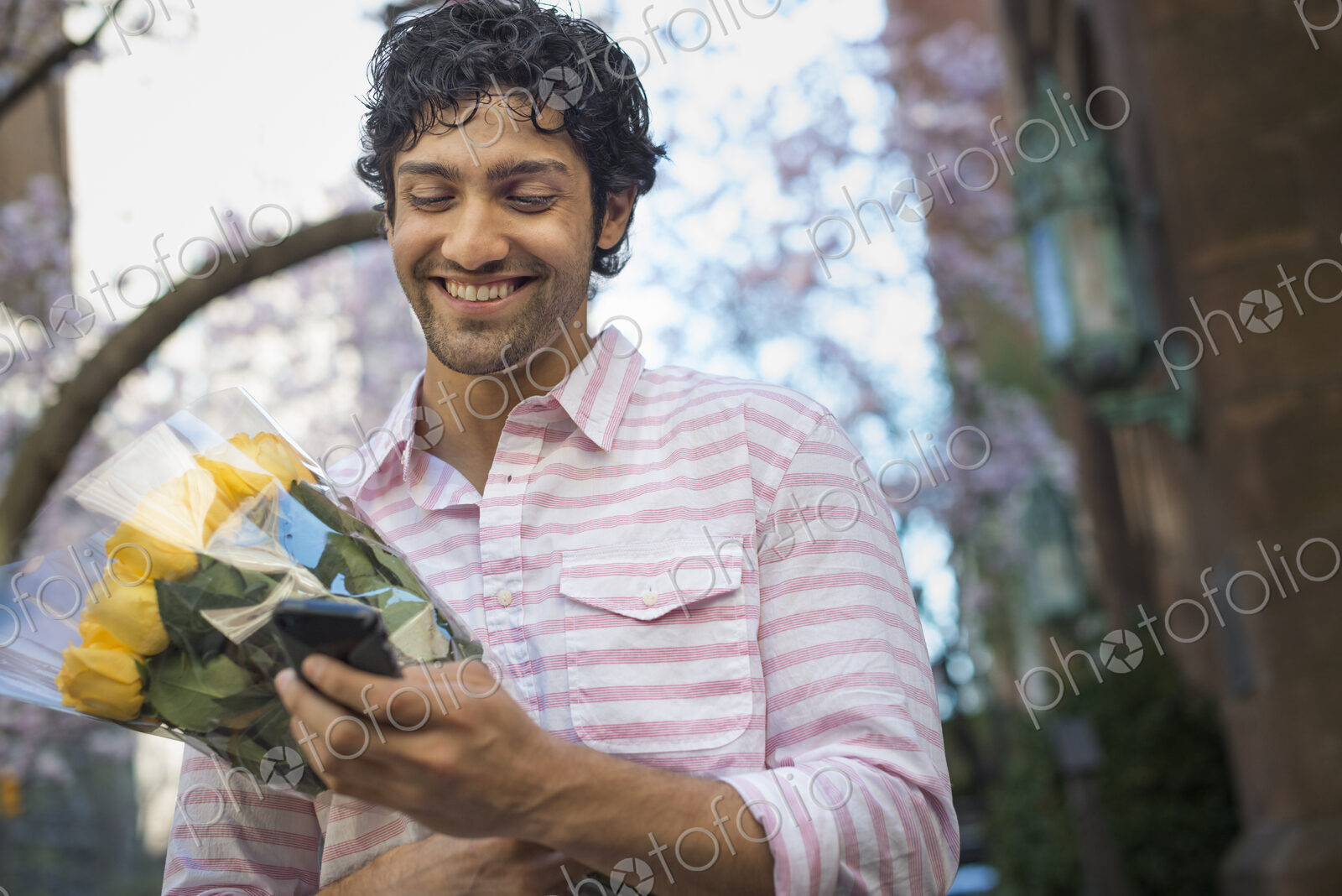 City life. A young man in the park in spring, using a mobile phone. Holding a bunch of…
