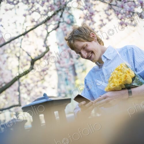 City life. A young man in the park in spring, using a mobile phone. Holding a bunch of…