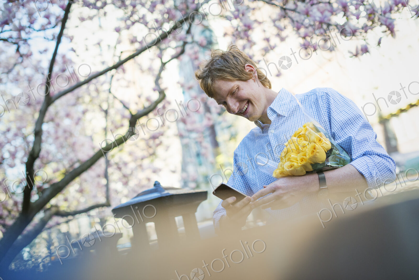 City life. A young man in the park in spring, using a mobile phone. Holding a bunch of…