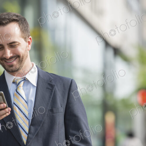 City life. People on the move. A man in a business suit checking his messages on his… City life. People on the move. A man in a business suit checking his messages on his…