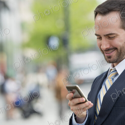 City life. People on the move. A man in a business suit checking his messages on his… City life. People on the move. A man in a business suit checking his messages on his…