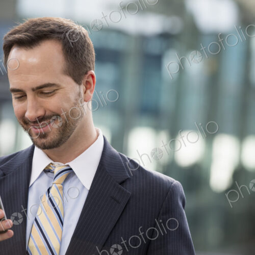 City life. People on the move. A man in a business suit checking his messages on his… City life. People on the move. A man in a business suit checking his messages on his…