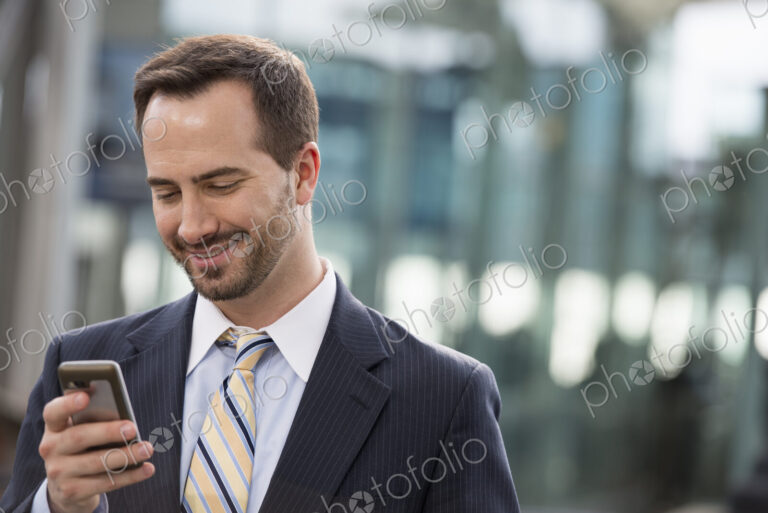 City life. People on the move. A man in a business suit checking his messages on his…